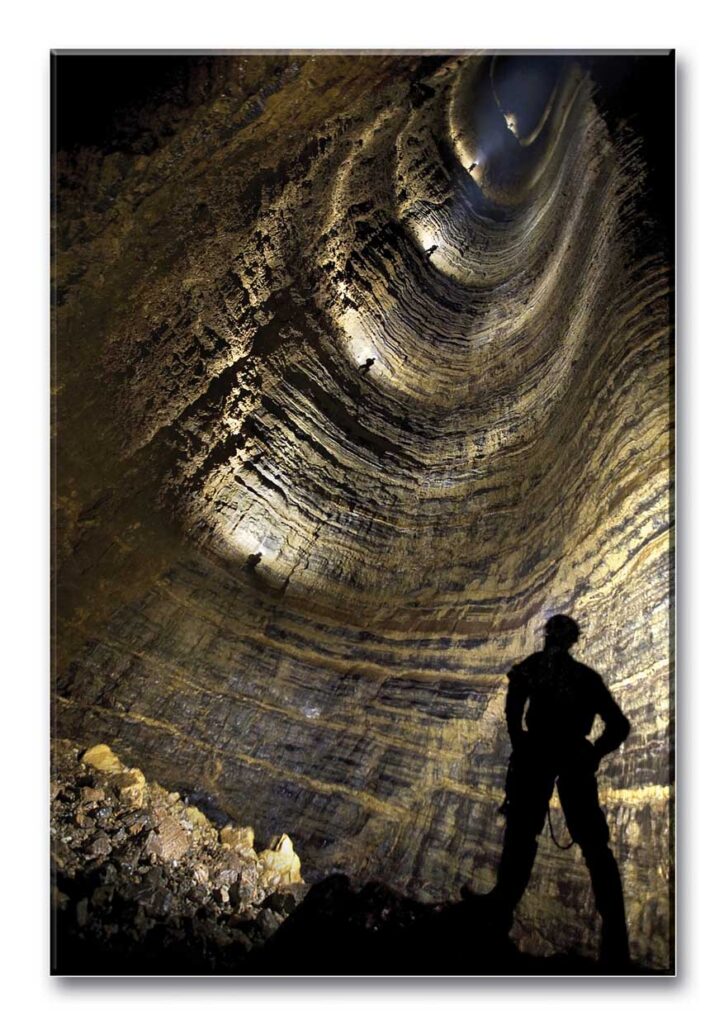 A caver in silhouette looks up at another caver climbing the Miao Keng shaft.